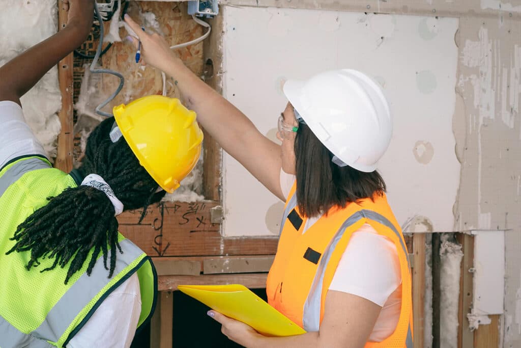 A supervisor guides a trainee through wiring work, showing on the job learning needed for electrician certification.