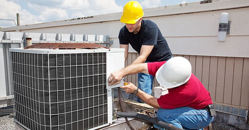 Two HVAC technicians repairing an air conditioning unit on a rooftop