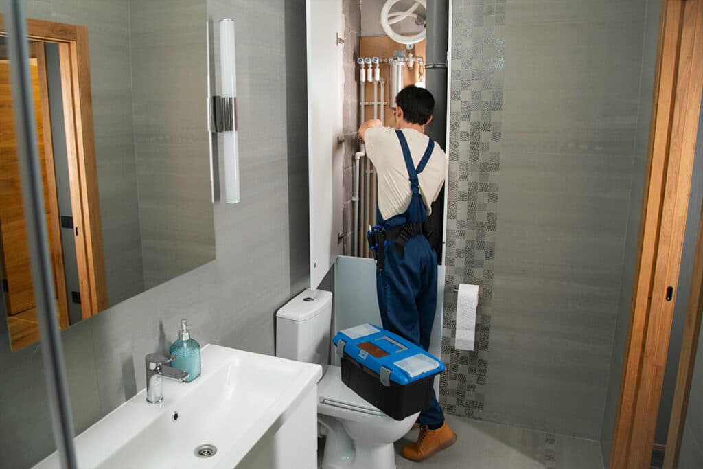 Plumber working on bathroom pipes, showcasing the type of work that influences plumber salary.