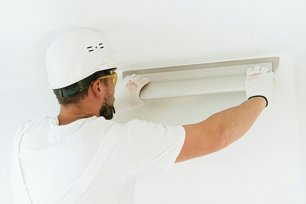 A technician installs a ceiling unit, performing hourly tasks included in an HVAC salary.