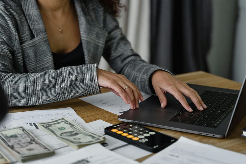 Person working on a laptop with electrician salary documents and printed reports on the desk.